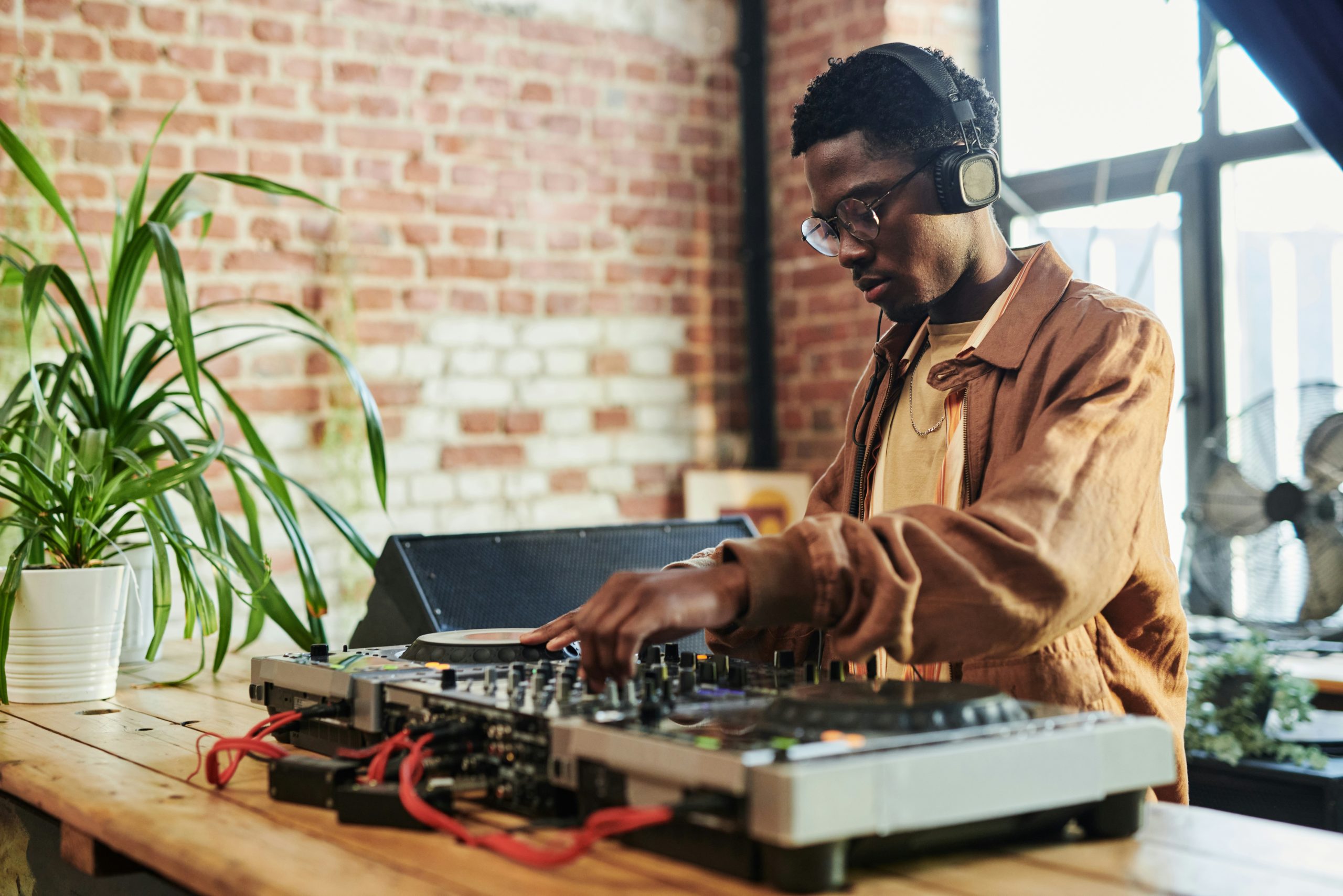 A music DJ indoors wearing headphones and using his turntables and mixer